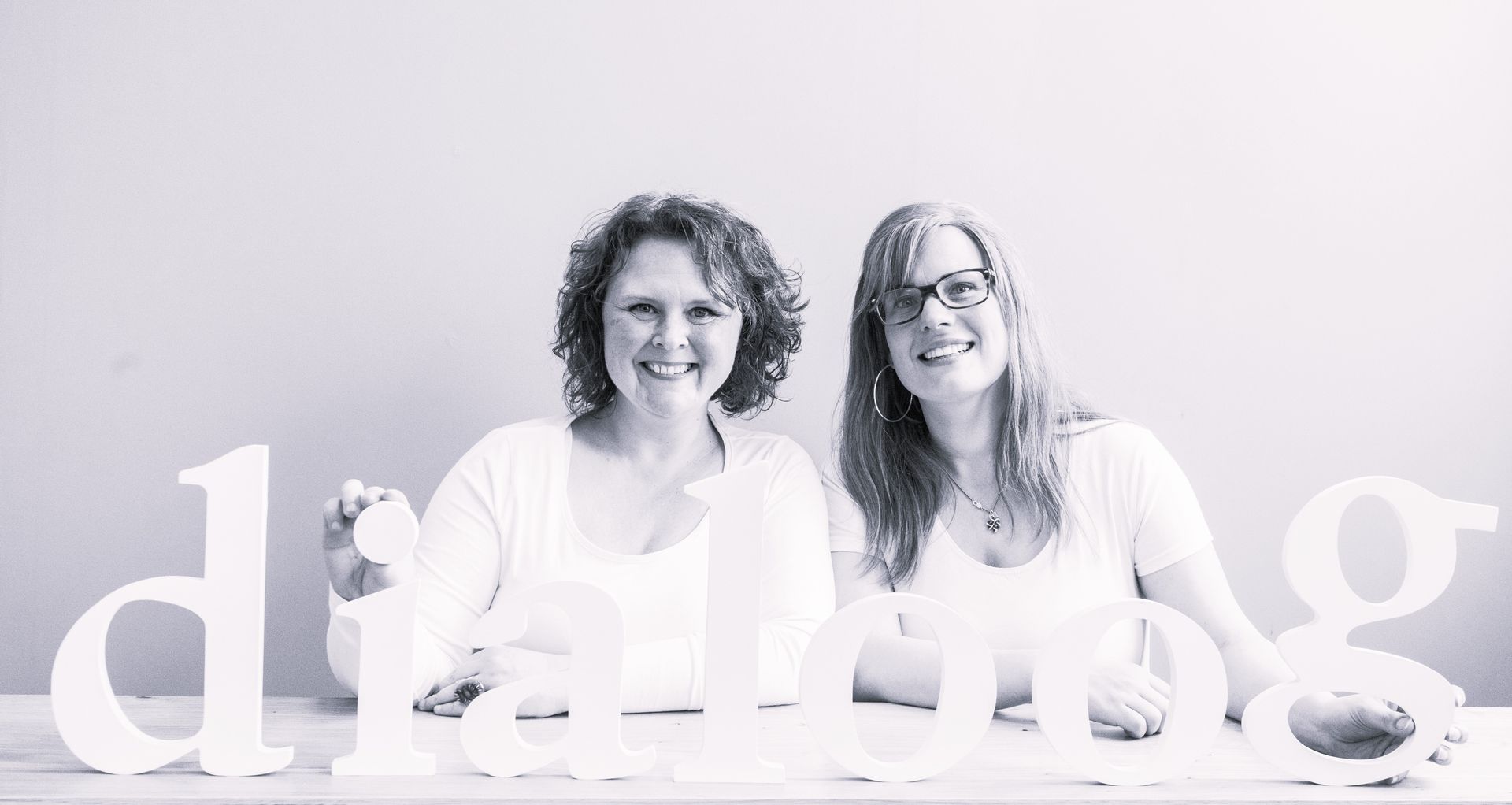 Twee vrouwen zitten aan een tafel en houden letters vast die het woord dansen vormen.
