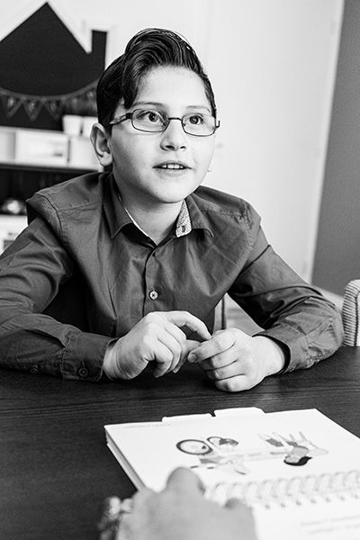 Een zwart-witfoto van een jonge jongen met een bril die aan een tafel zit.