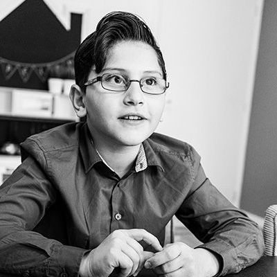 Op een zwart-witfoto zit een jonge jongen met een bril aan een tafel.