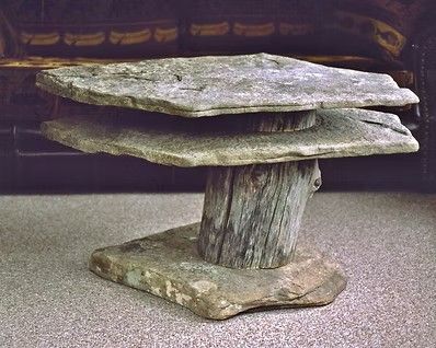 Stone table with a thick slab top and central carved support on a gravel surface