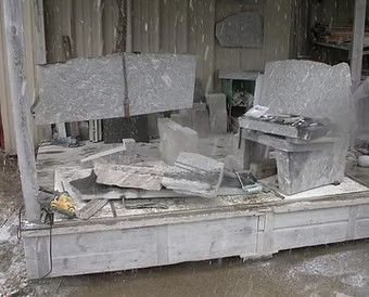 Stone carving workshop with large gray sculpted blocks and debris on a dusty platform