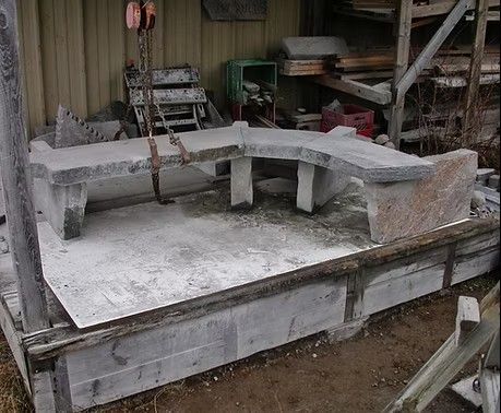 Stone bench sections chained on a wooden platform in a workshop yard