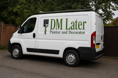 White DM Later Painter and Decorator van parked on a street beside trees and a brick wall