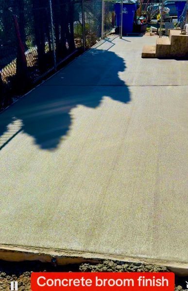 Concrete path with broom finish, in an outdoor setting. The surface is gray with shadows and a retaining edge.