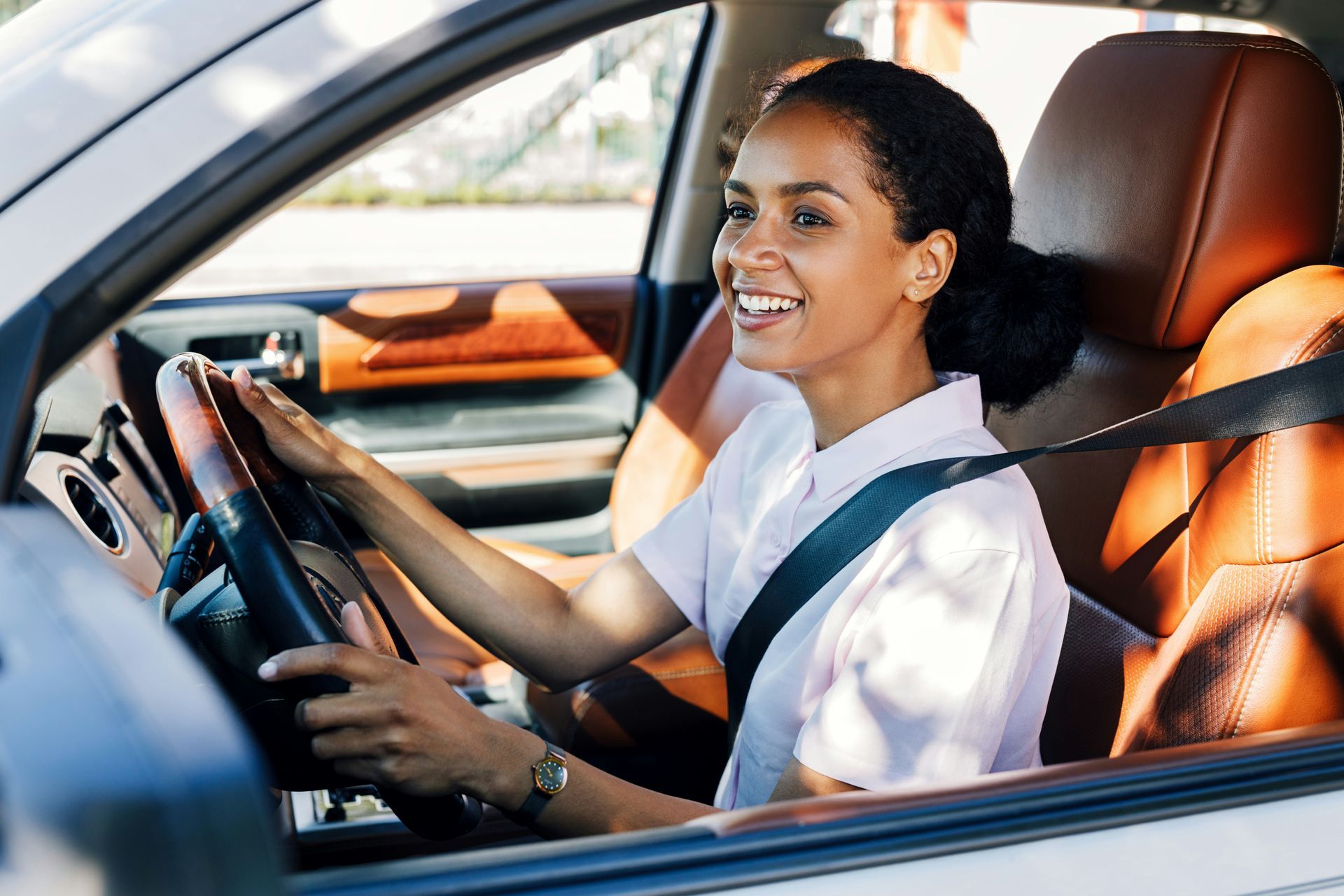 A woman is sitting in the driver 's seat of a car and smiling.