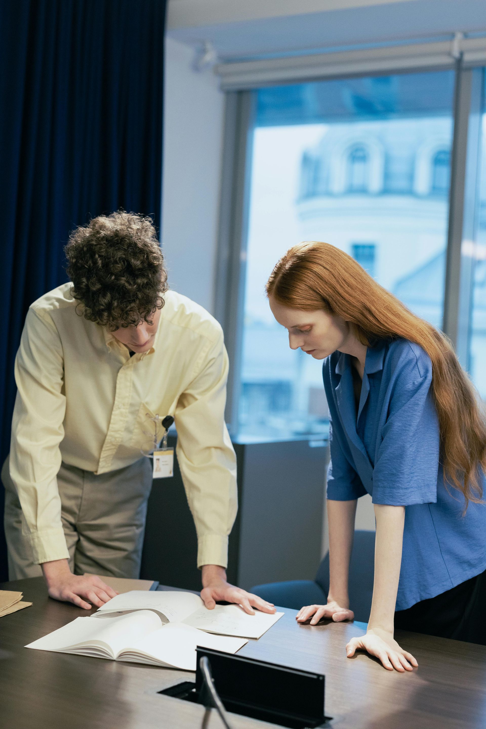 A man and a woman are standing at a table looking at a book.