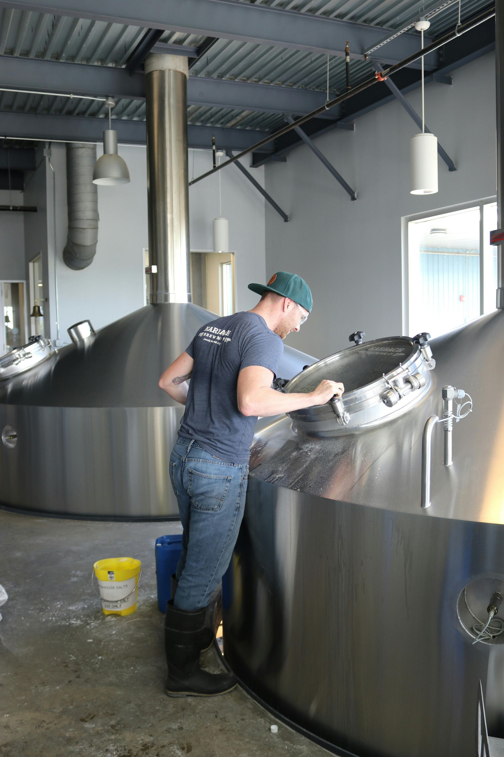 A man is working on a large metal tank in a brewery.