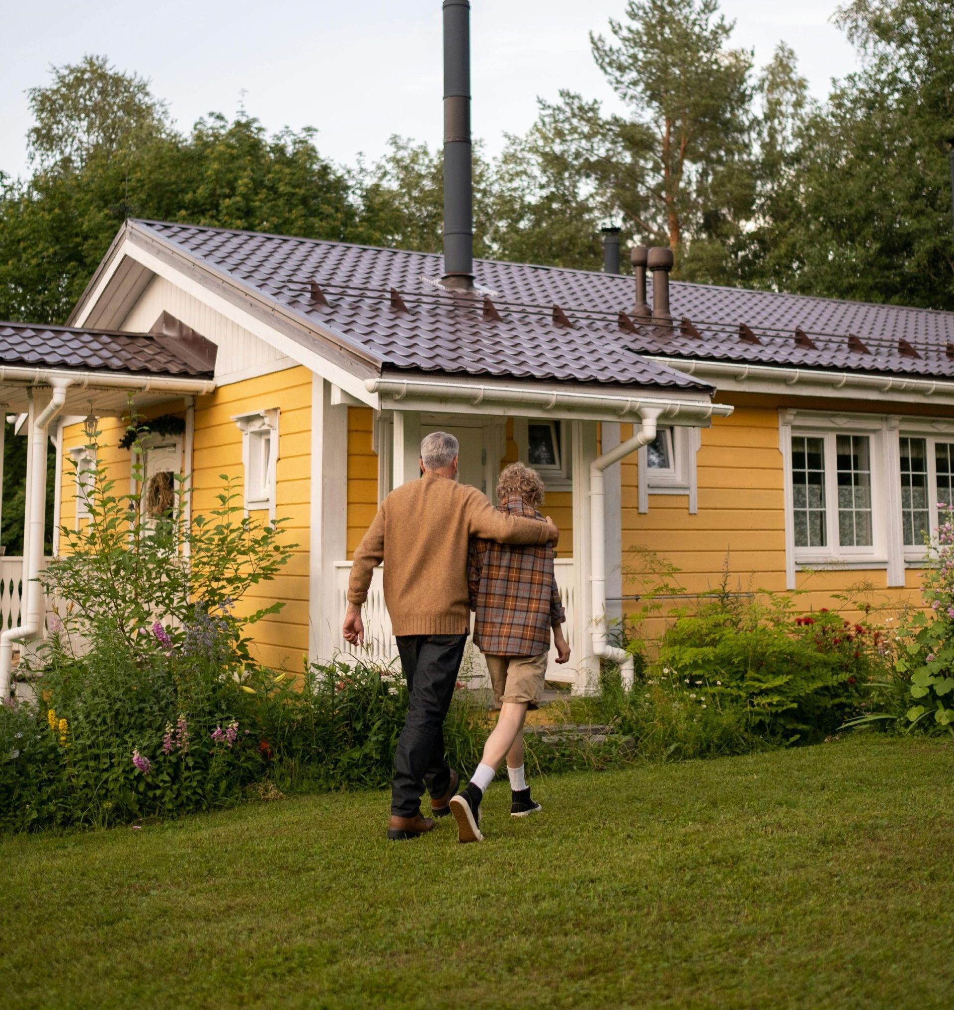 A man and a boy are walking towards a yellow house