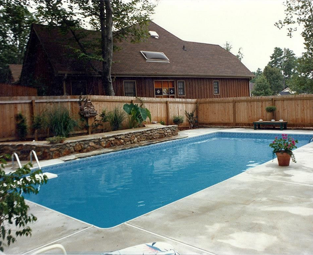 Infinity pool overlooking a valley at sunset. Poolside patio with lounge chairs; trees frame the view.