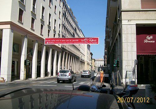 Via cittadina con auto parcheggiate, edifici e uno striscione rosso teso attraverso la carreggiata.
