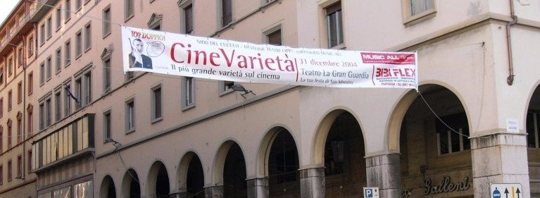 Lo striscione di CineVarietà è appeso sopra un porticato stradale su un edificio color beige.