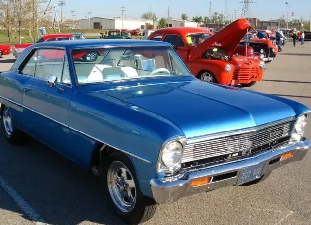 A blue car with the hood up is parked in a parking lot