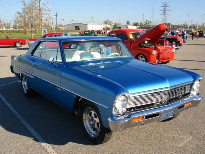 A blue car with the hood up is parked in a parking lot