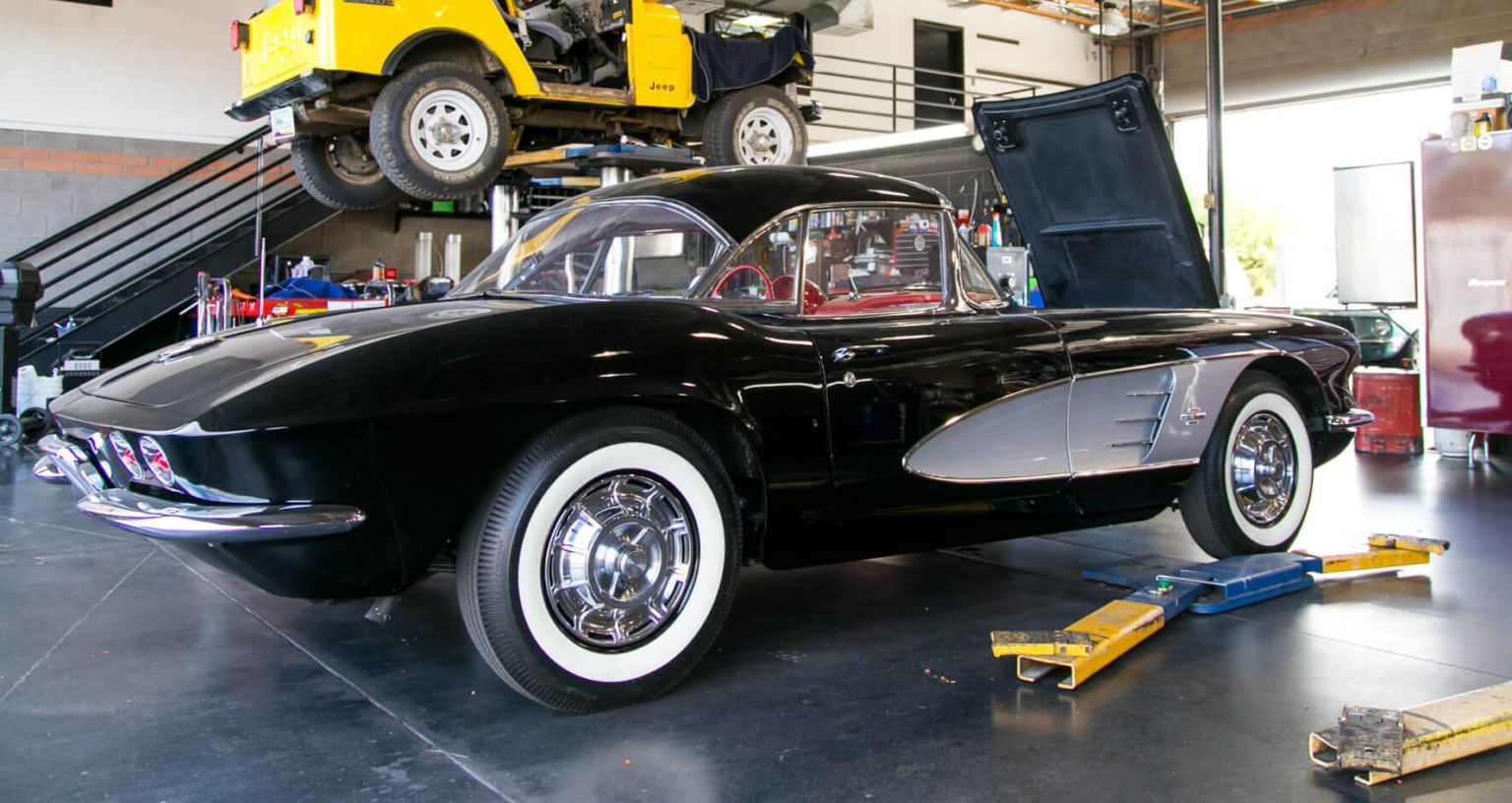 A black car with white tires is on a lift in a garage.