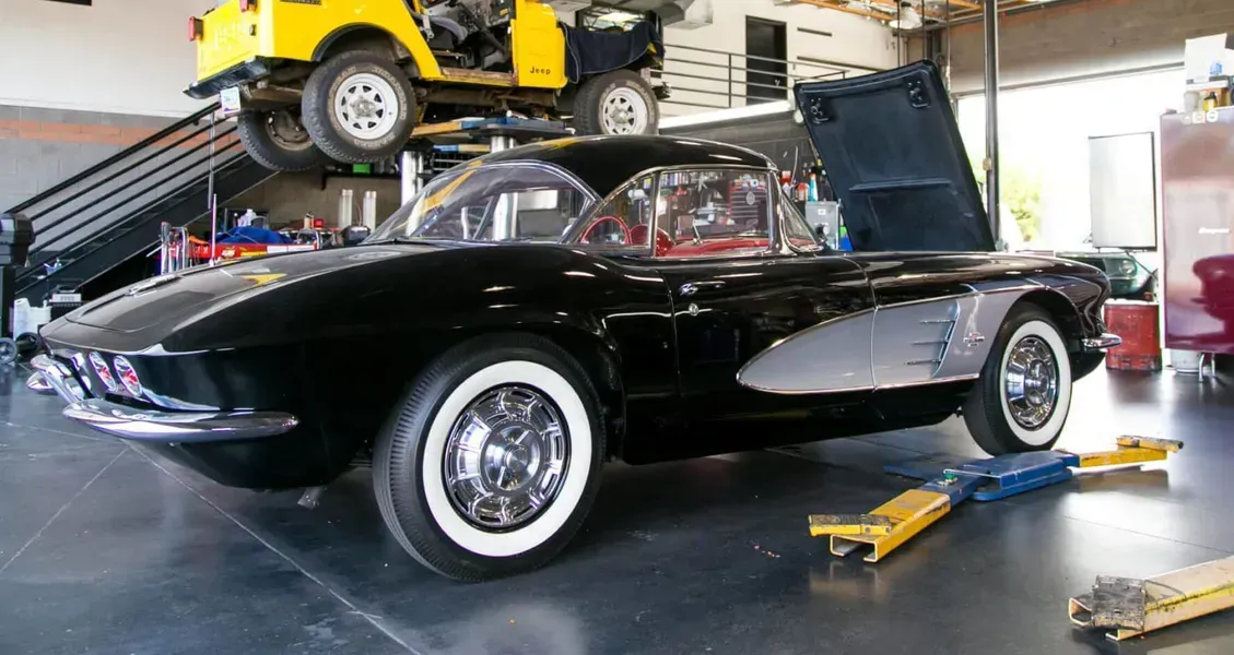 A black corvette is sitting on a lift in a garage.