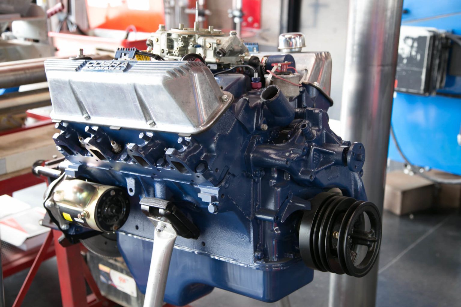 A blue engine is sitting on a stand in a garage.