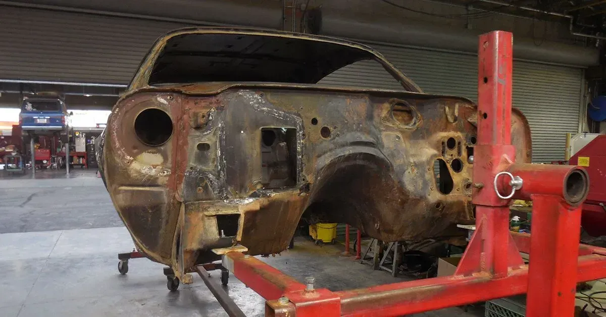 A rusty car is sitting on a red stand in a garage.
