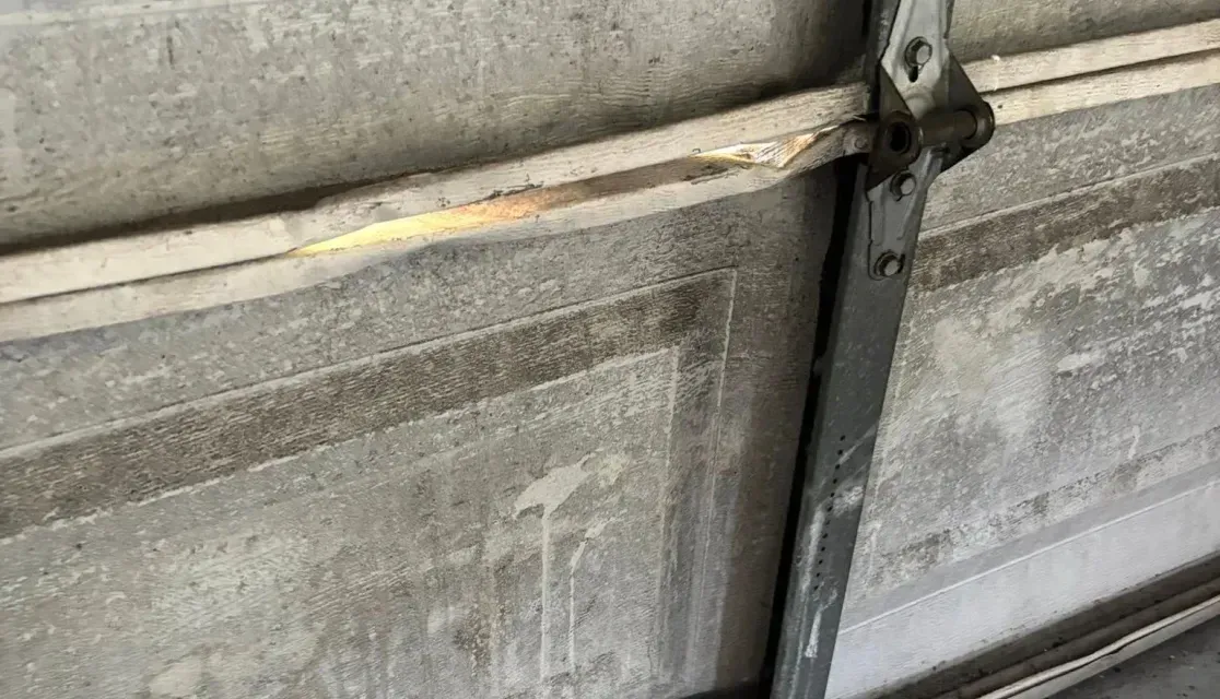 Close-up of a damaged garage door hinge with a bent metal brace and scuffed concrete floor.