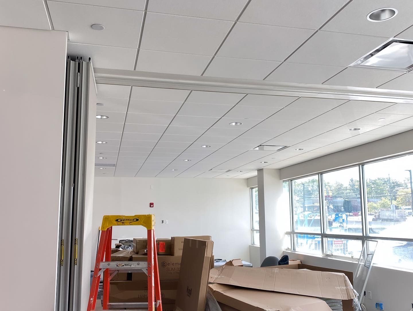 Interior room with construction in progress. Boxes, ladder, and white walls. Bright overhead lighting.