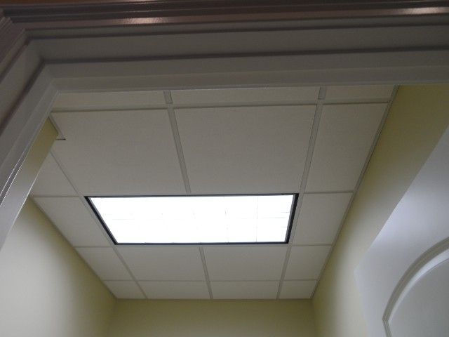 View looking up at a drop ceiling with a rectangular fluorescent light fixture. White and beige tones.