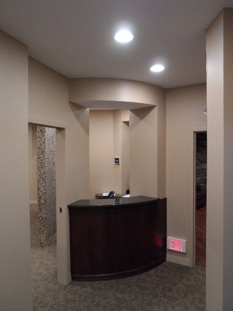 Reception area with dark wooden desk, recessed lighting, and beige walls.