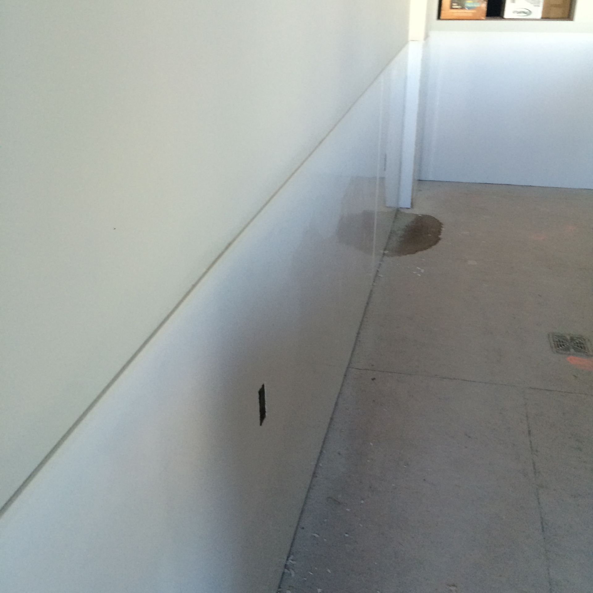 White wainscoting on wall with electrical outlet, concrete floor.