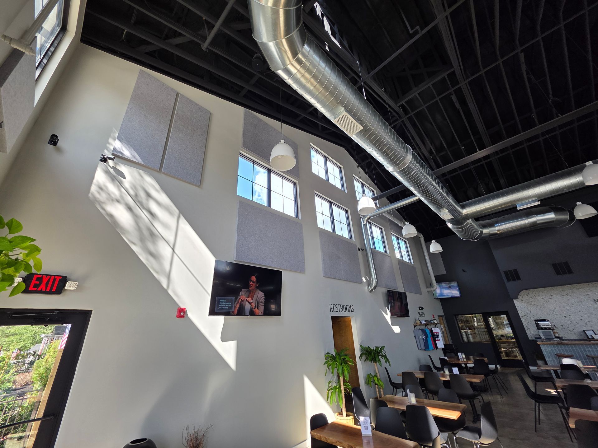 Interior of a modern building with high ceilings, featuring acoustic panels, windows, and tables.