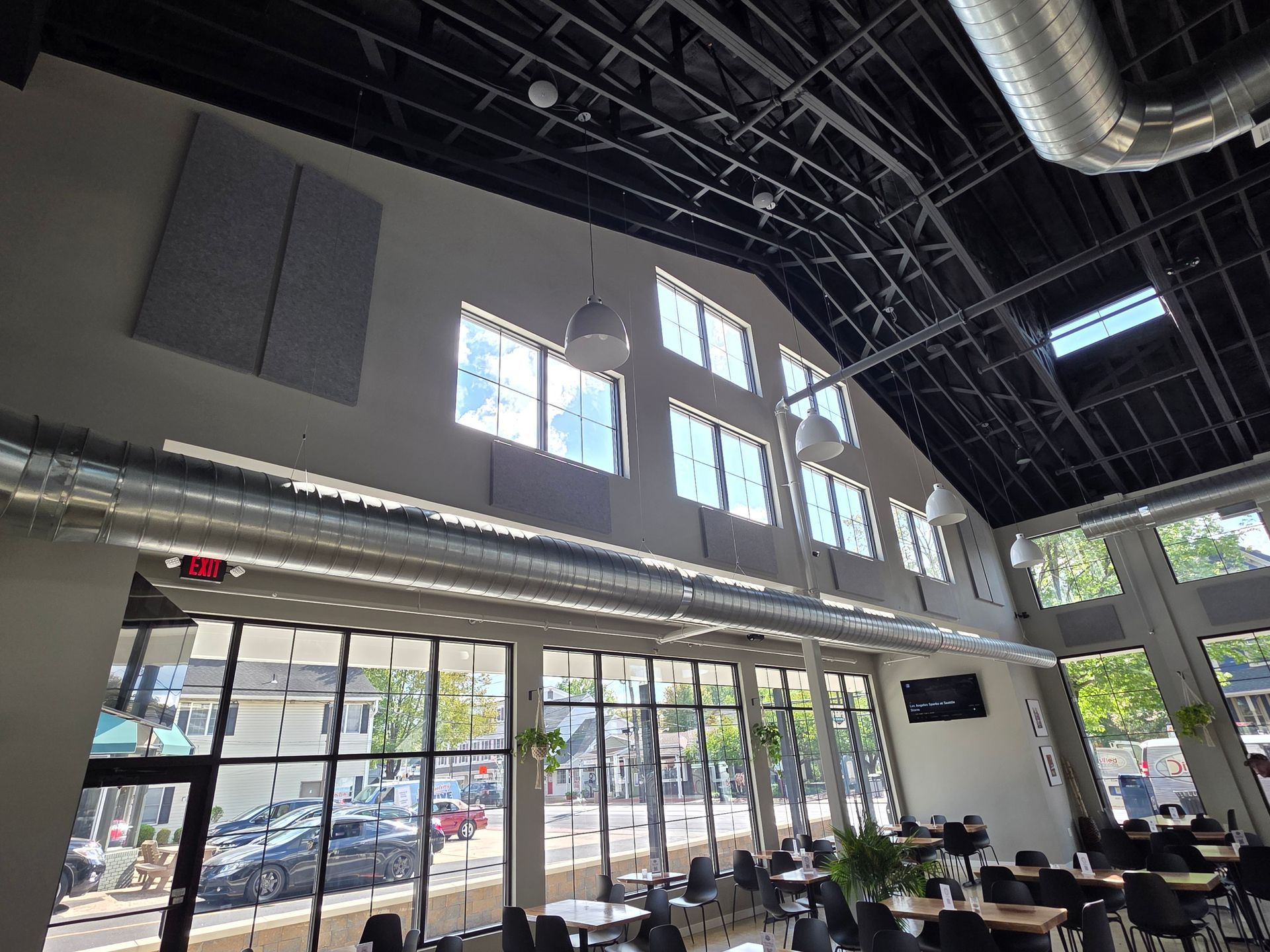 Interior view of a modern restaurant with large windows, black ceiling, and exposed ductwork, overlooking a city street.