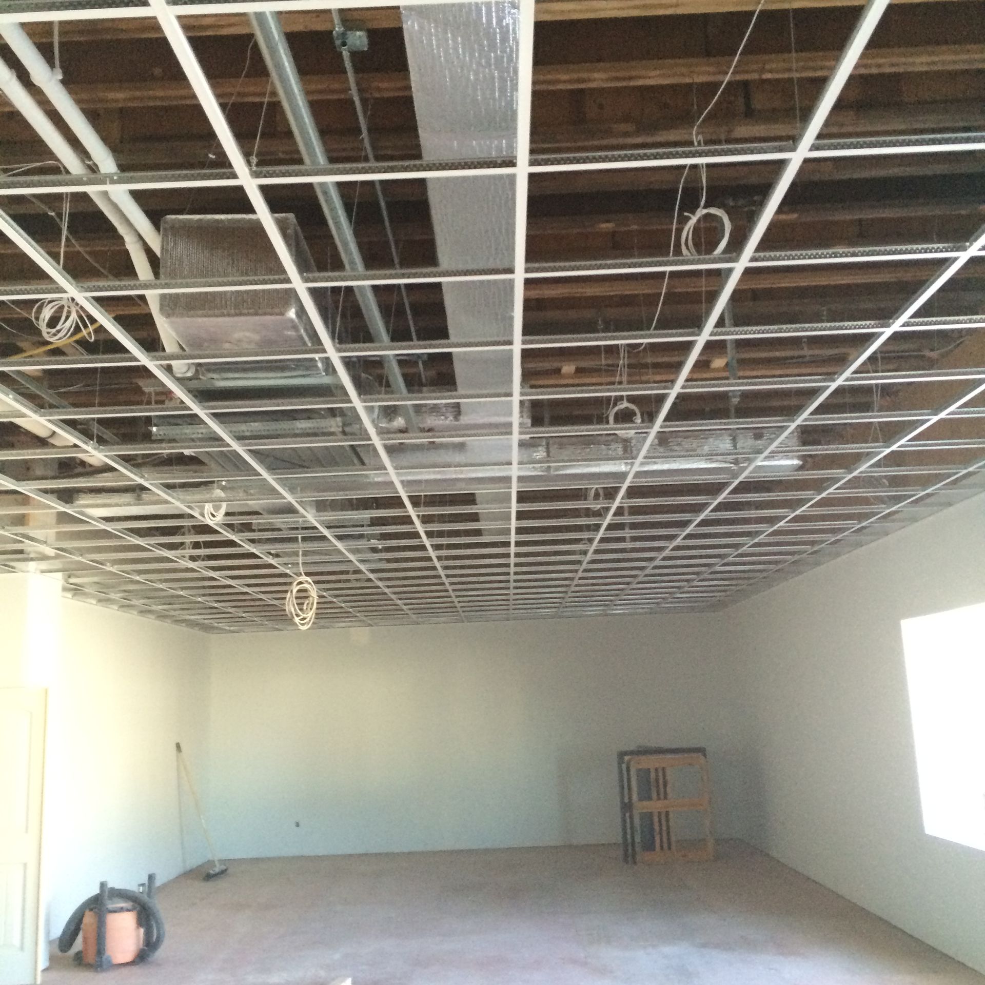 Interior of a room under construction; exposed ceiling grid, wires, bare walls, and unfinished floor.