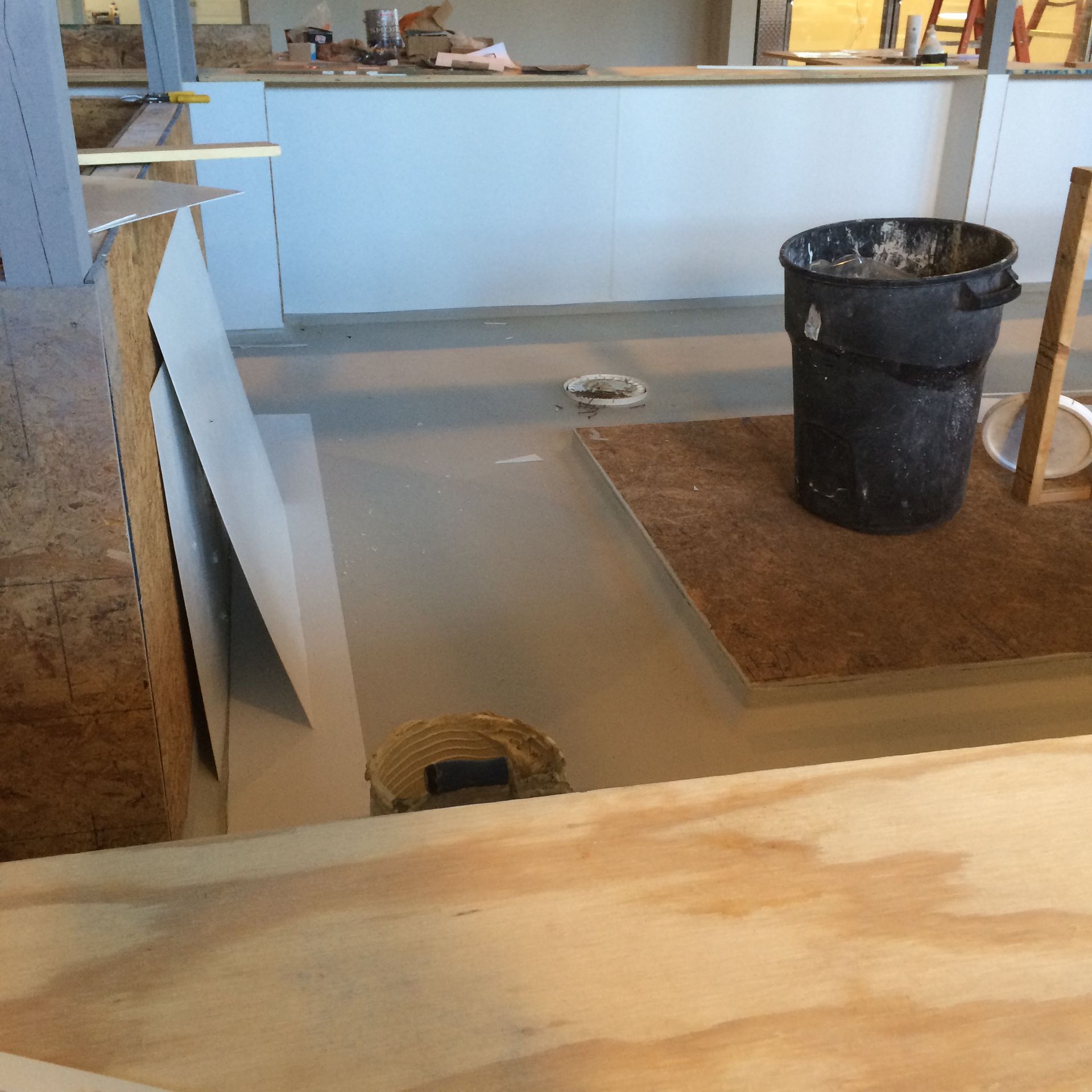 Construction site with a gray-painted floor, a black trash can, and building materials.