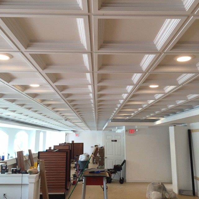 Cream-colored coffered ceiling with recessed lighting in an unfinished office space; tools and cubicles are present.