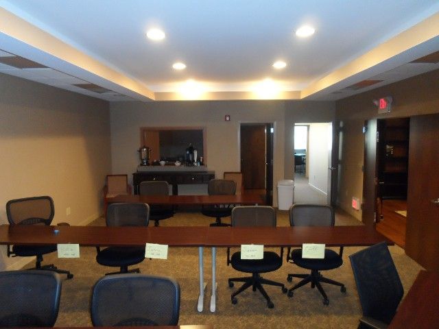 Conference room with long table, chairs, and coffee station. Beige walls, recessed lighting.