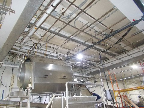 Industrial ceiling with pipes, wires, and equipment. A stainless steel tank sits below.
