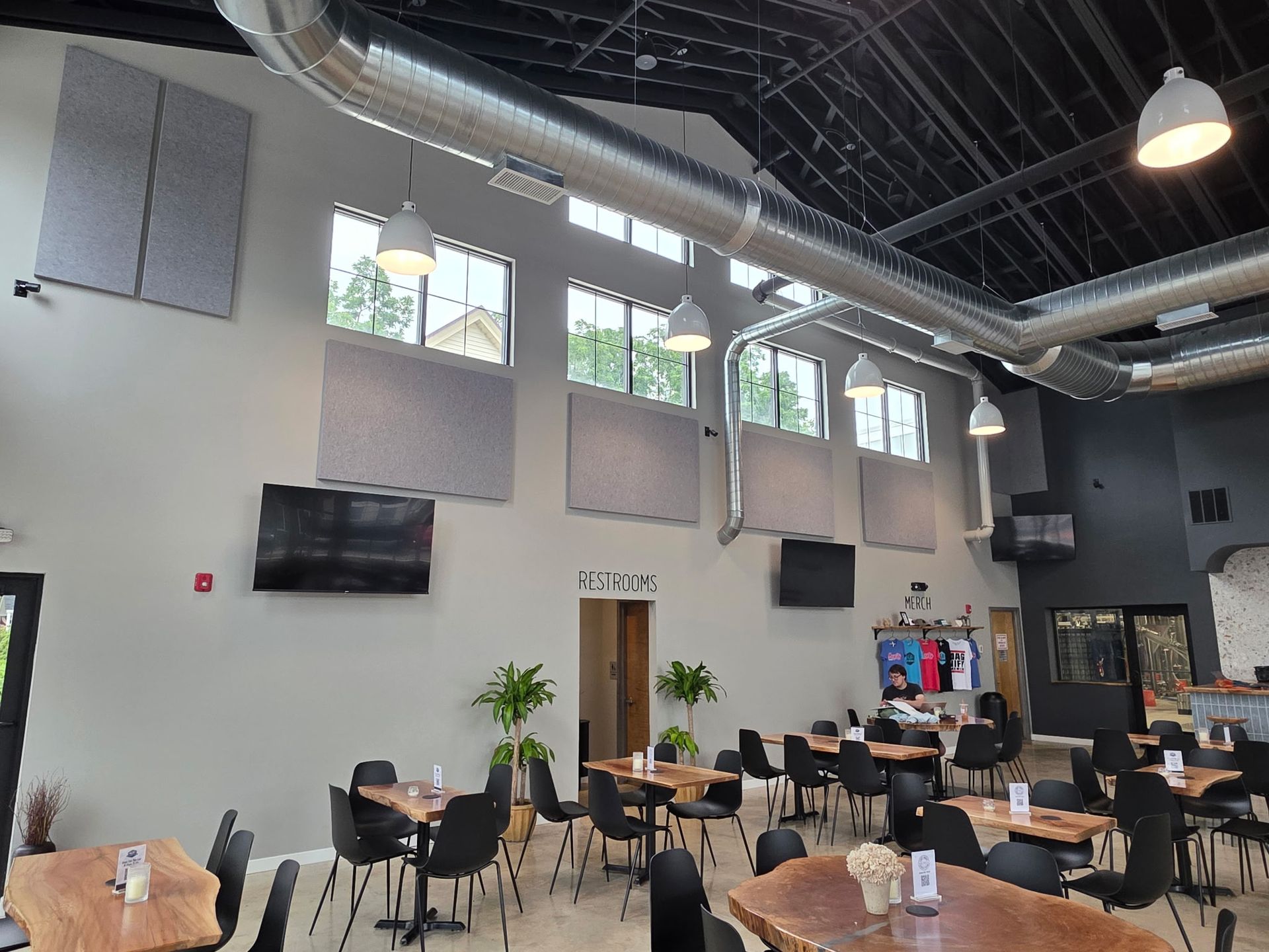 Interior of a restaurant with tables, chairs, windows, TVs, and air ducts.