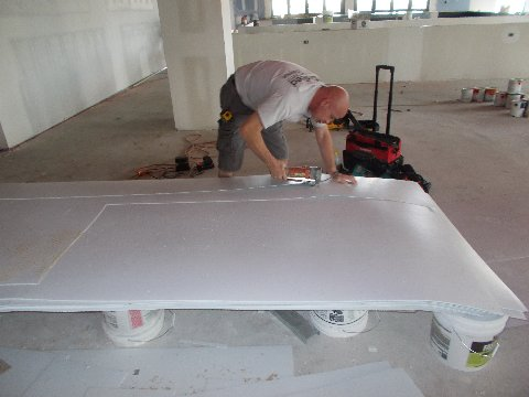 Man using a tool on a large white sheet, supported by buckets in a construction setting.