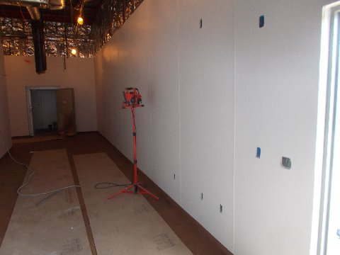 Construction interior: white walls, exposed ceiling, red work light, doorway, and flooring under construction.