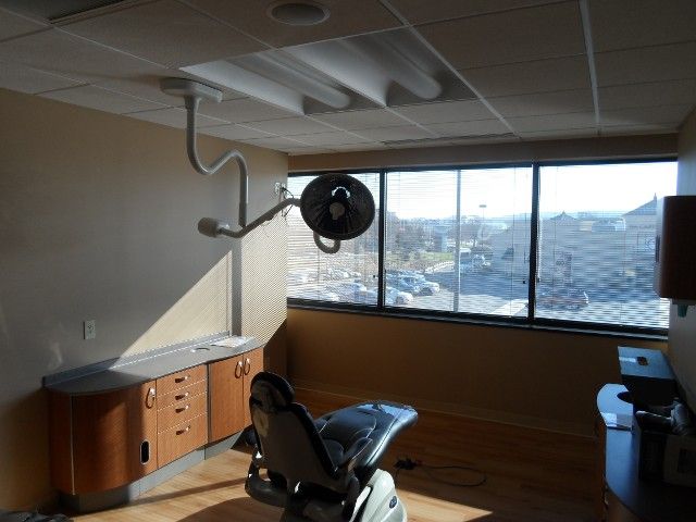 Dental office room with dental chair, cabinets, and window overlooking a parking lot.