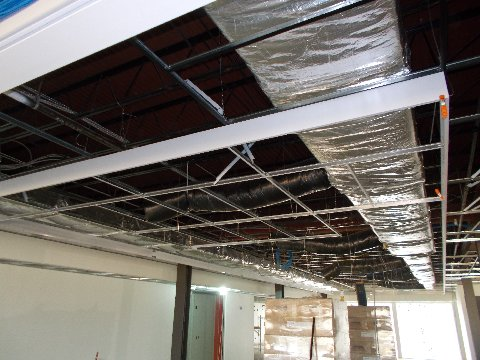 Interior ceiling under construction, metal grid with ductwork and support beams.