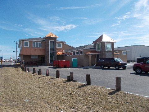 Building with copper-colored roofs and turrets under construction on a sunny day with parked vehicles.
