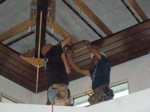 Two workers installing brown wooden ceiling panels.