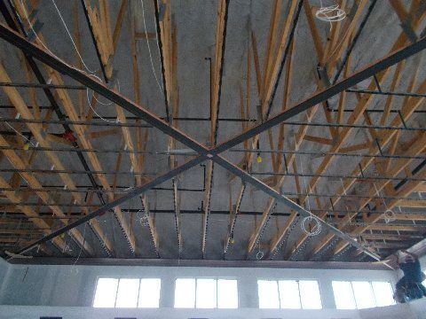 Wood and metal ceiling structure in a large room, with exposed beams and crossbars.