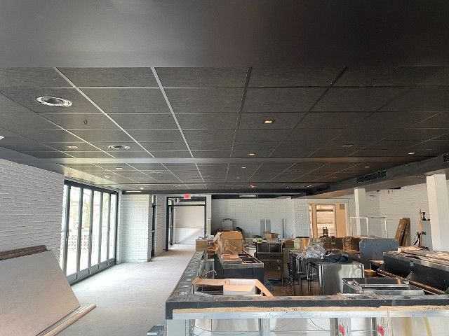 Interior of a commercial space under construction, featuring a black tiled ceiling, bar area, and large windows.