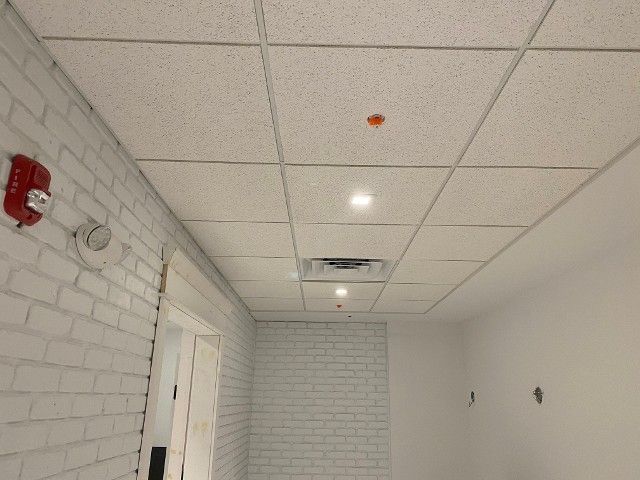 White brick wall, drop ceiling, hallway with fire alarm, lights, and open vent.