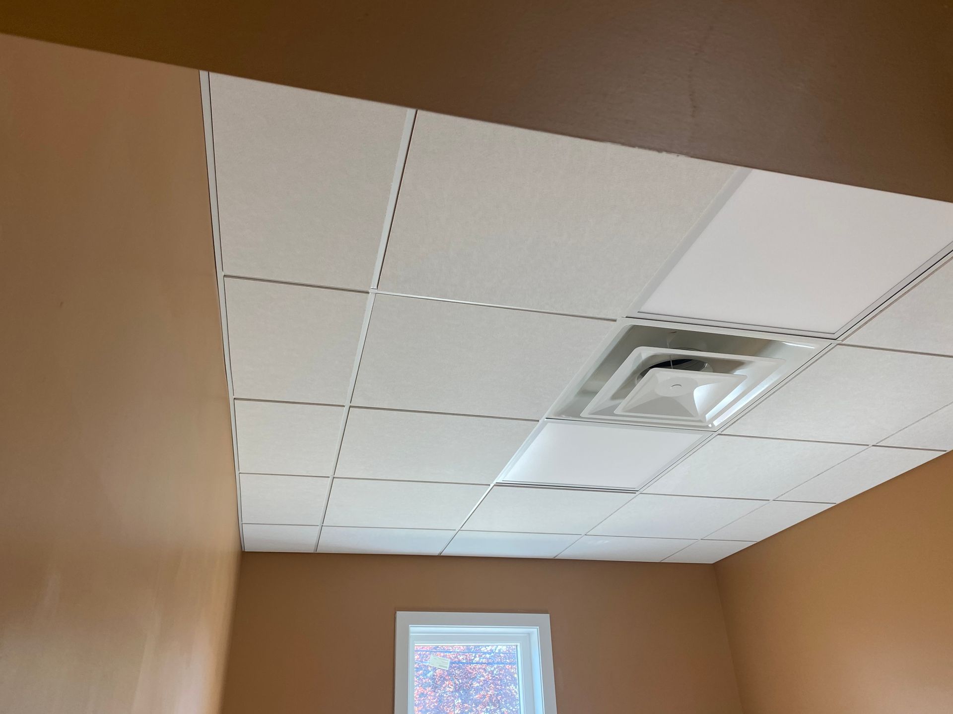Ceiling with white tiles, air vent, and tan walls.