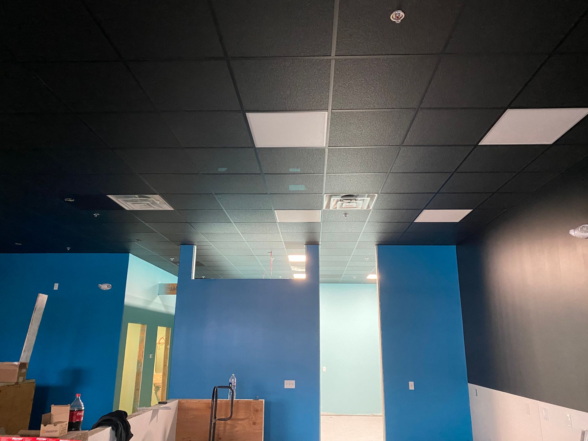 Interior view of a room under construction with blue walls, black ceiling tiles, and white ceiling lights.