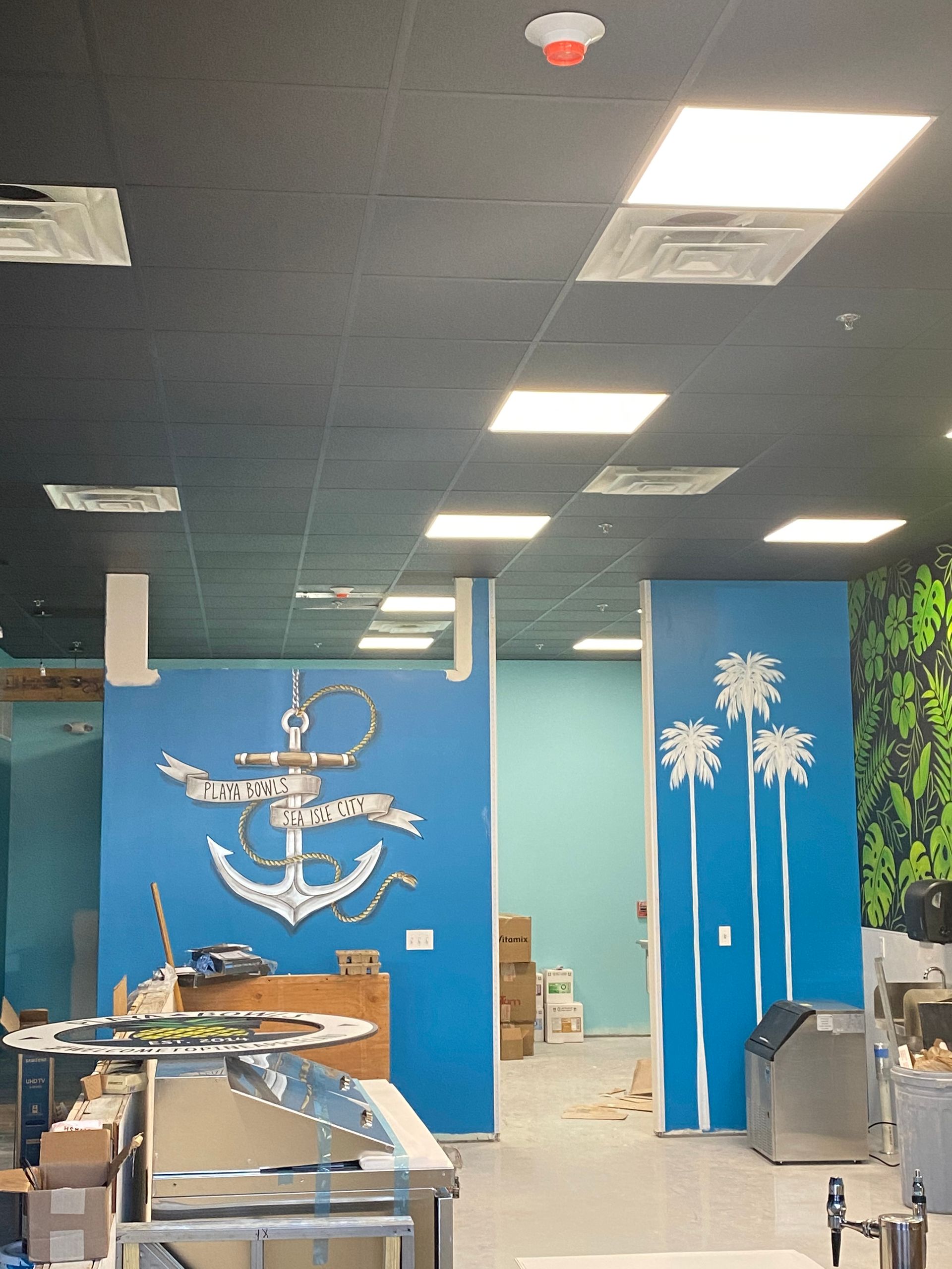 Interior with blue walls, an anchor mural, and palm tree designs; commercial space under construction.