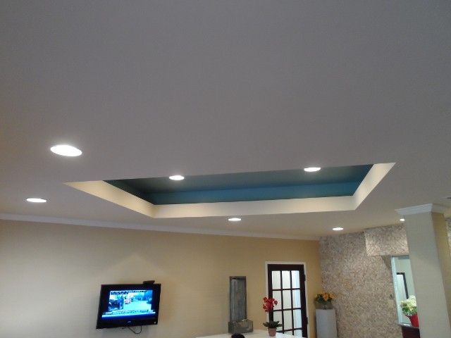 Living room ceiling with recessed area painted blue, surrounded by white ceiling and recessed lights, TV on wall.