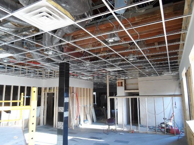 Interior of a building under construction, showing exposed ceiling grid, framing, and unfinished walls.