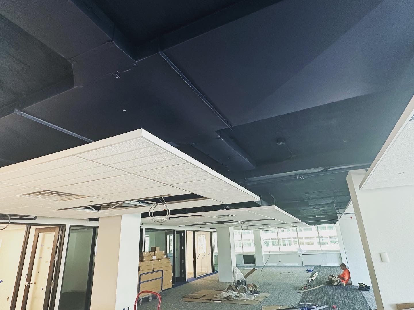 Interior view of an office space under construction with a dark blue ceiling and exposed wires.