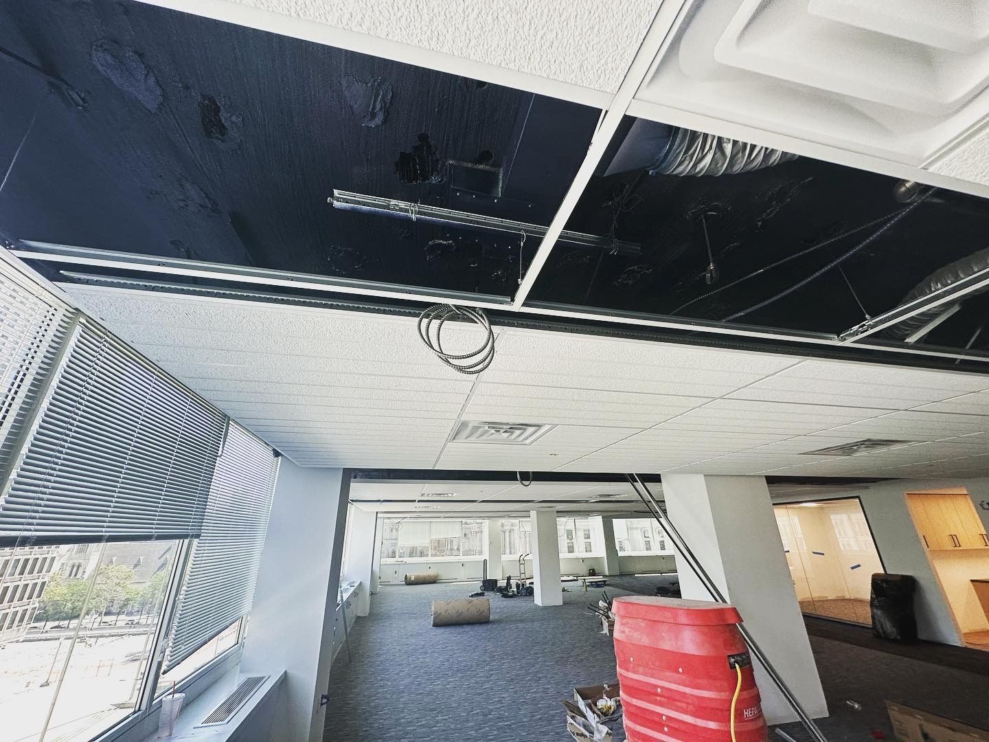 Office interior with exposed ceiling tiles, damaged ceiling, open space, and building materials.